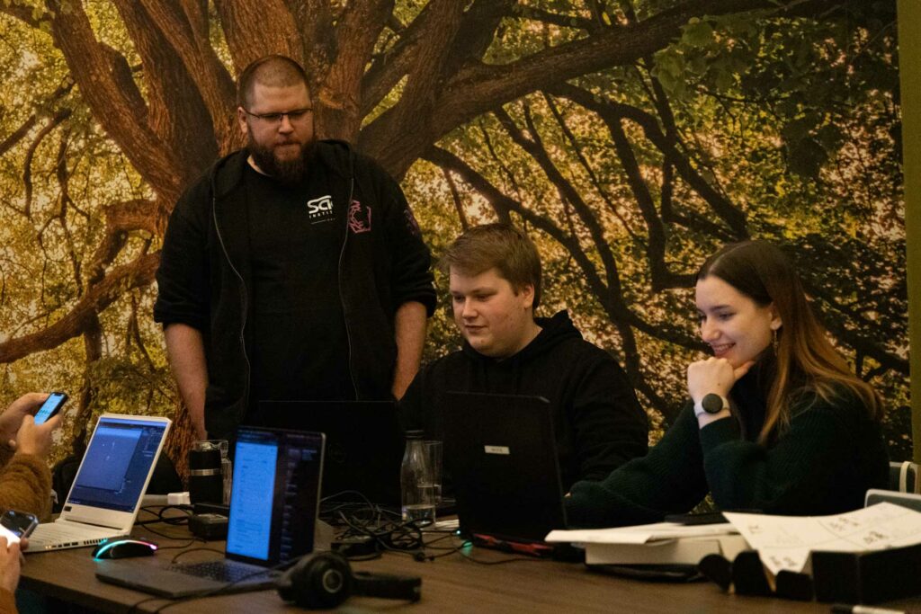 Studenten sitzen zusammen am Tisch und arbeiten. Hinter ihnen eine Waldtapete.
