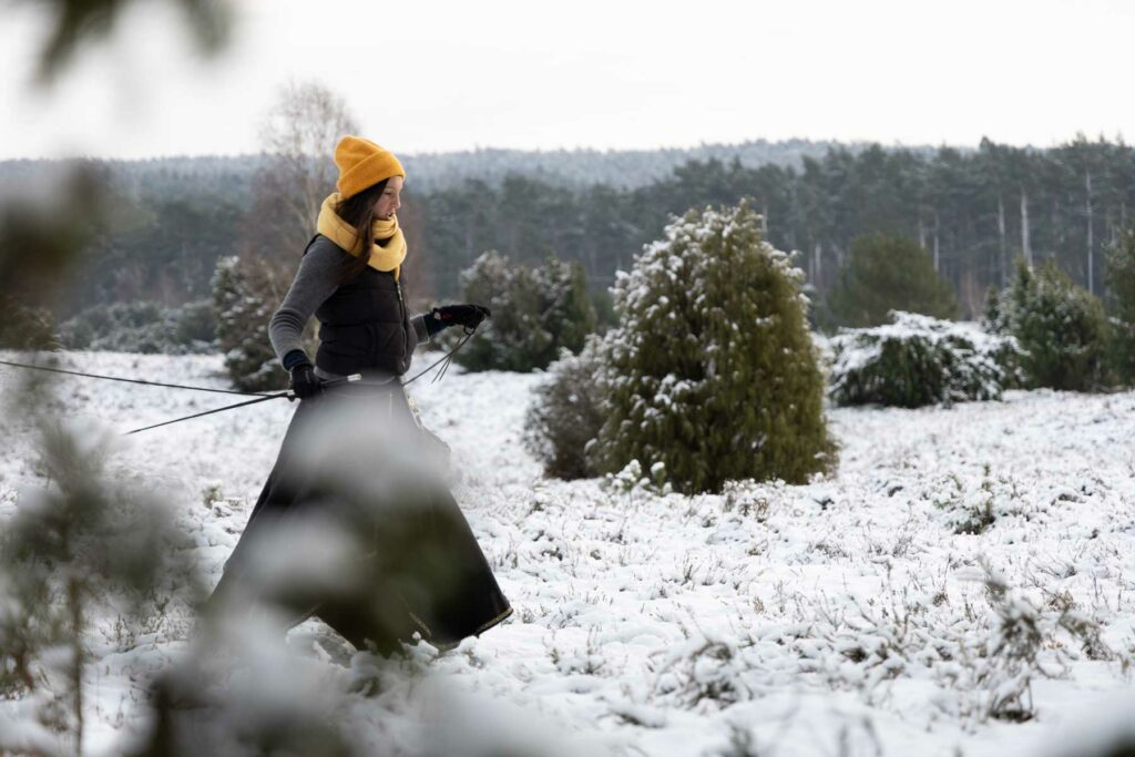 Frau mit gelber Mütze läuft durch verschneite Landschaft