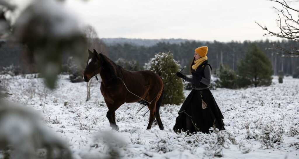 Frau läuft mit Pferd durch eine verschneite Landschaft.
